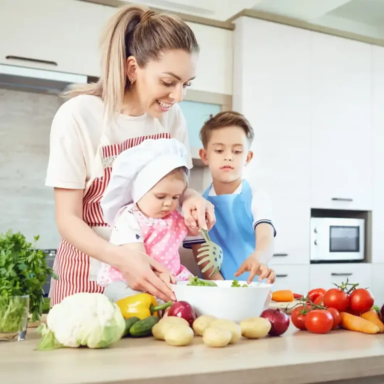 Mealpreprezepte für die ganze Familie Eine Frau kocht mit zwei Kindern, umgeben von frischem Gemüse in einer modernen Küche.