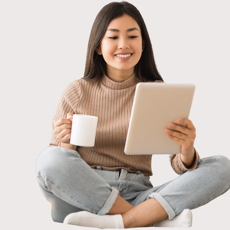 Momlifebalanced Shop Frau sitzt mit Tablet und Kaffeetasse, lächelnd und in entspannter Haltung.